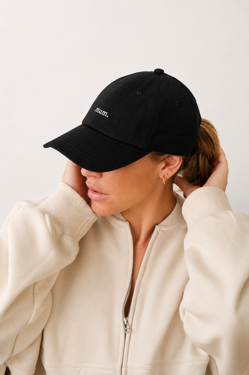 Person wearing a black cap with 'mum' printed on it, against a plain background