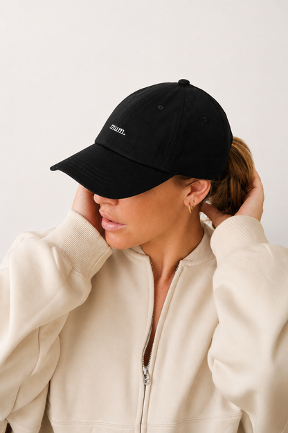 Person wearing a black cap with 'mum' printed on it, against a plain background