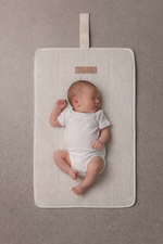Newborn baby lying on a beige bouclé change mat by Little & Co with logo detail in a neutral setting