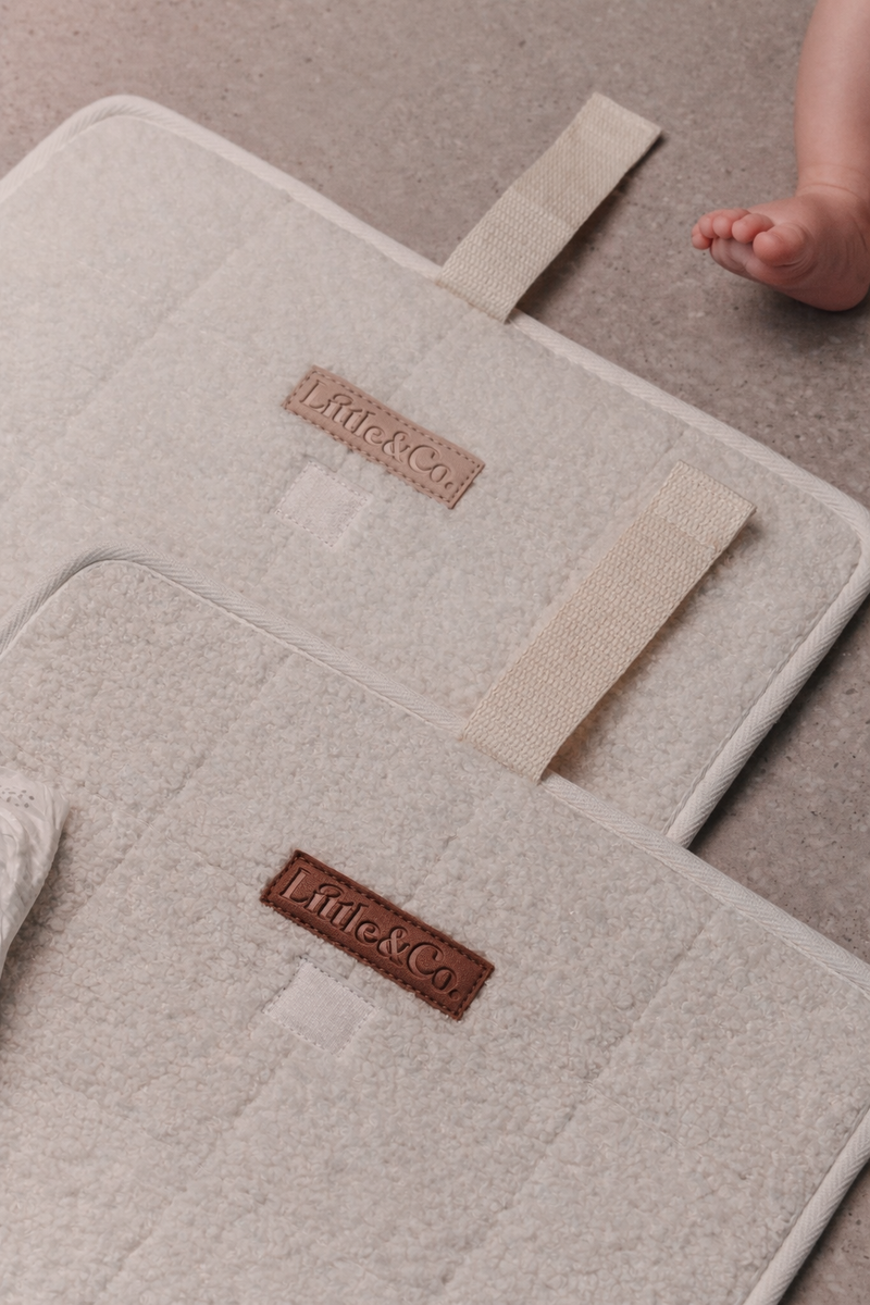 Close-up of beige Little & Co bouclé change pads with logo detail, with a baby’s foot visible in the background.