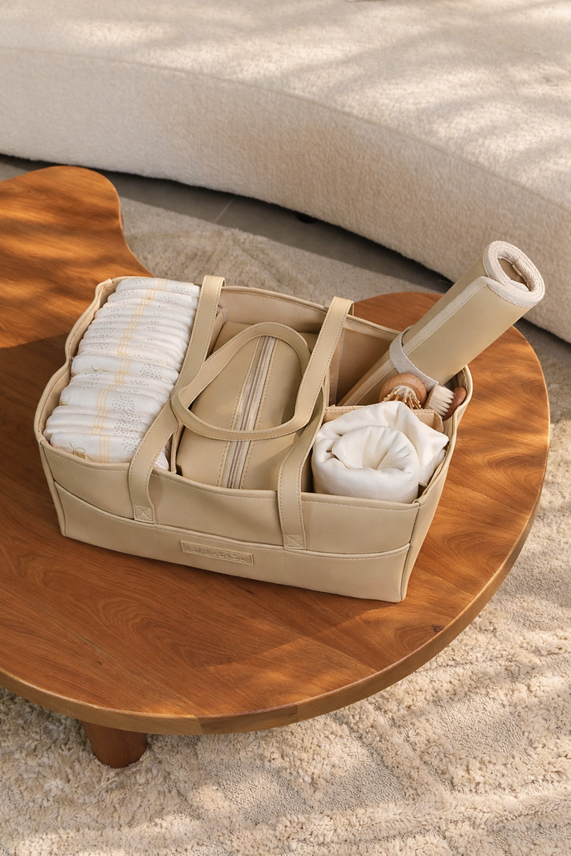 Beige leather Little & Co nappy caddy organised with baby essentials on a wooden table in a neutral living space.