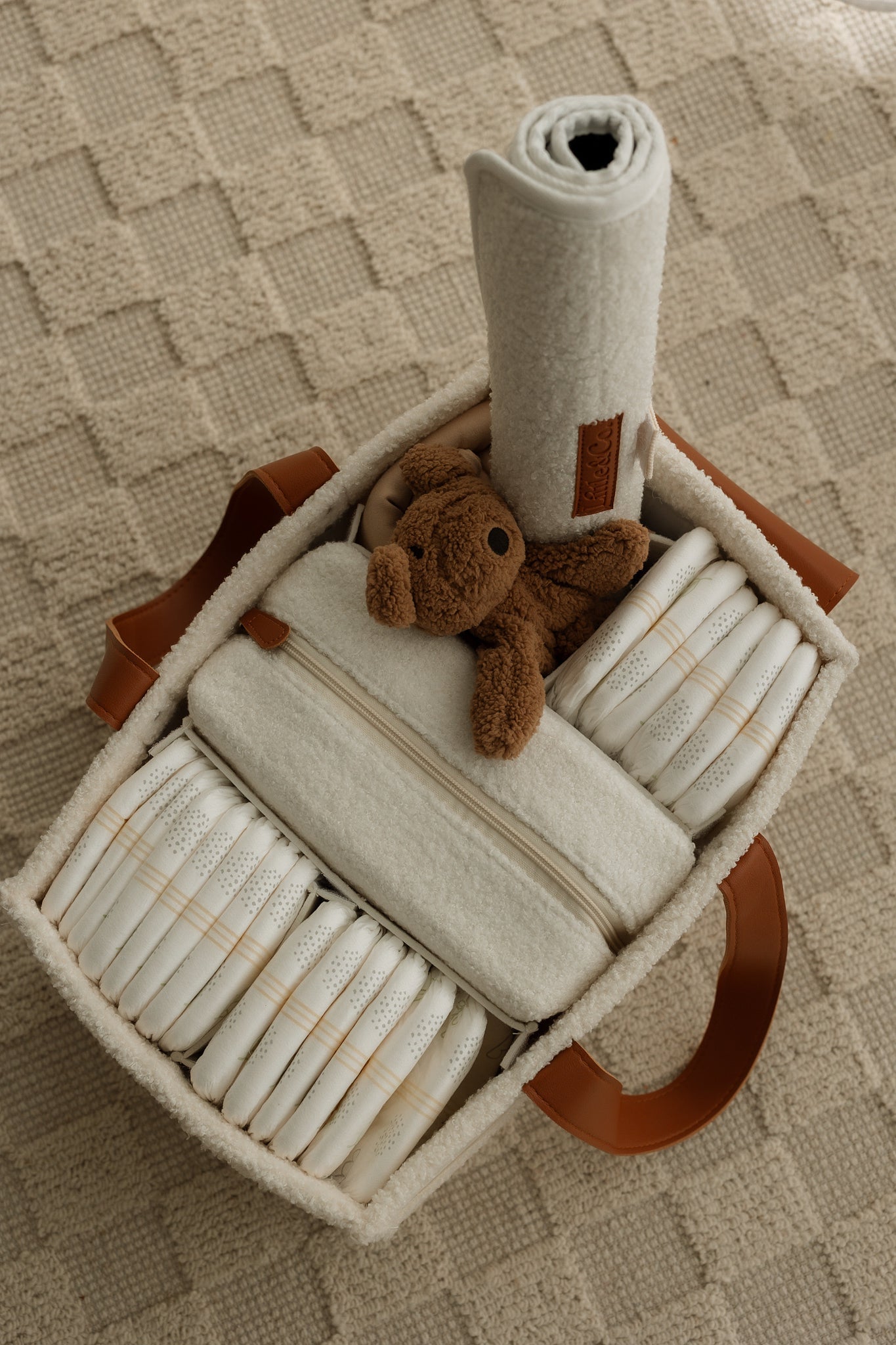 Nappy caddy filled with baby items including diapers, a blanket, and a teddy cuddly.