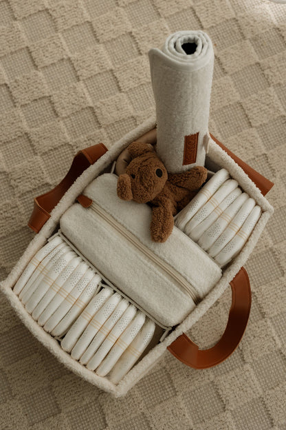 Nappy caddy filled with baby items including diapers, a blanket, and a teddy cuddly.