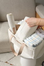 Person holding a folded blanket with a neutral color scheme on a couch.