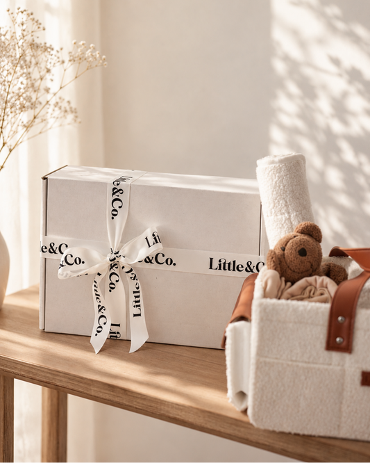 White gift box with 'Little & Co.' ribbon and teddy bear on a wooden surface.