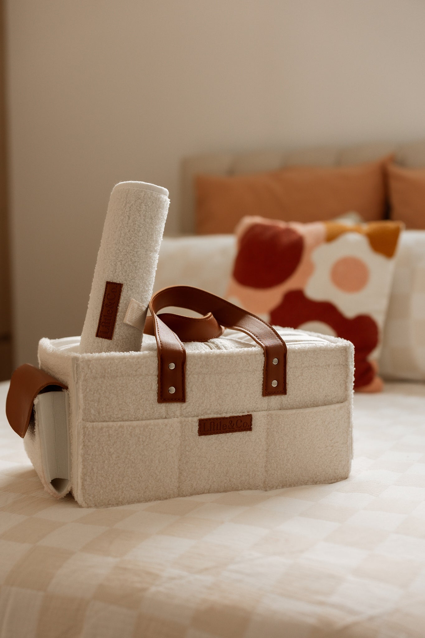 cream boucle caddy with brown straps on a bed with colorful pillows in the background