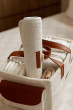 Cream bouclé baby nappy caddy with tan leather handles, neatly organised with nappies and essentials, featuring a rolled cream changing mat with a Little & Co logo on top.