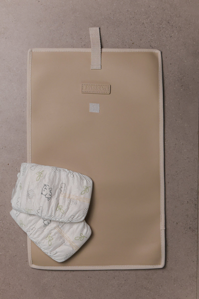 Beige leather baby change mat by Little & Co with nappy placed on top, styled on a neutral background.