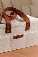 Close-up of a cream bouclé nappy caddy with tan leather handles and Little & Co logo, filled with nappies and baby essentials.
