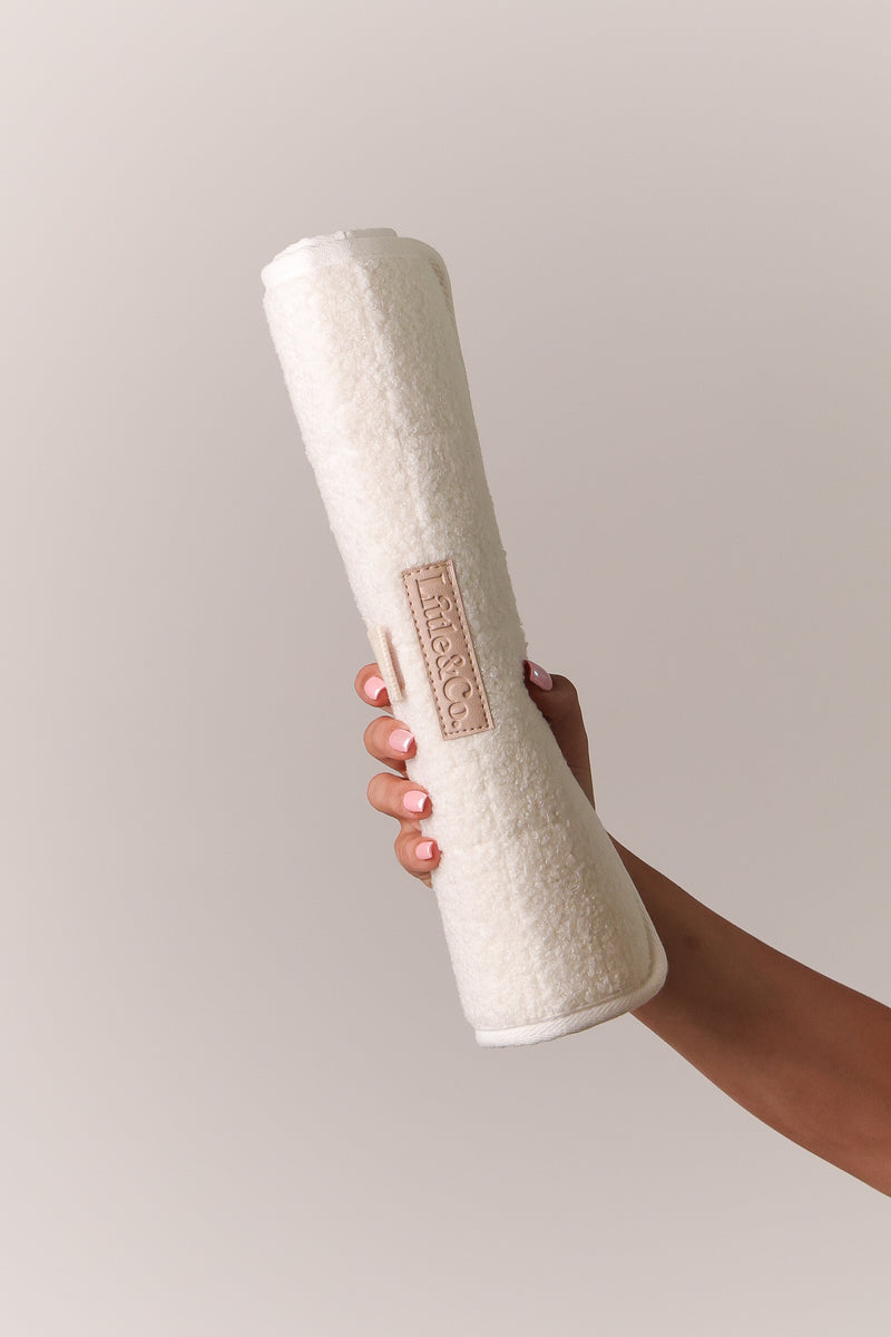 Hand holding a rolled beige bouclé change mat by Little & Co against a clean neutral background