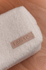 Close-up of a folded beige bouclé baby blanket with Little & Co logo label on a wooden surface