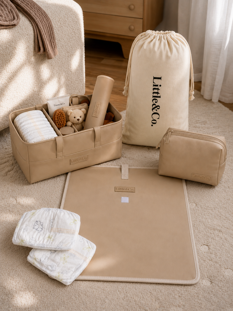 Baby care products including a changing mat, diapers, and a bag with 'Little & Co.' branding on a wooden floor.