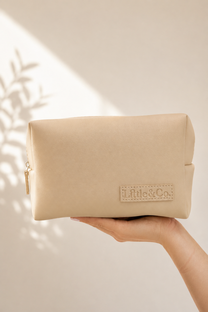 Beige pouch held by a hand Little & Co.' branding on a neutral background