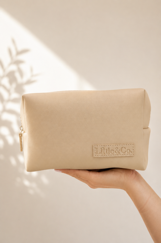 Beige pouch held by a hand Little & Co.' branding on a neutral background