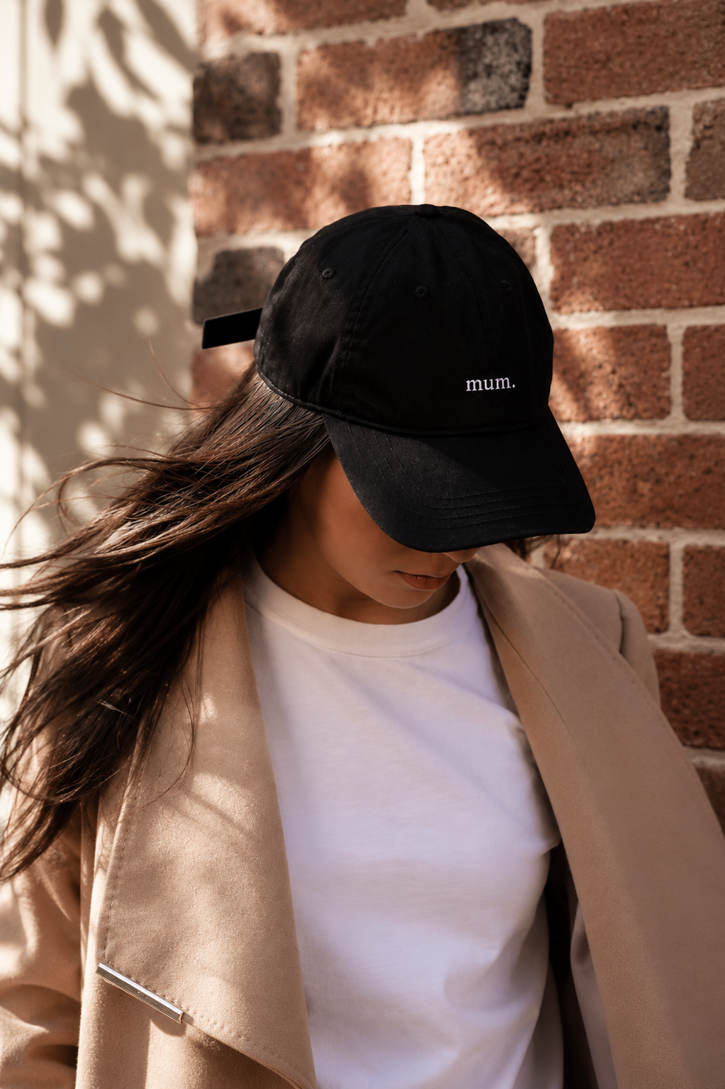 Person wearing a black cap with 'mum.' text against a brick wall.