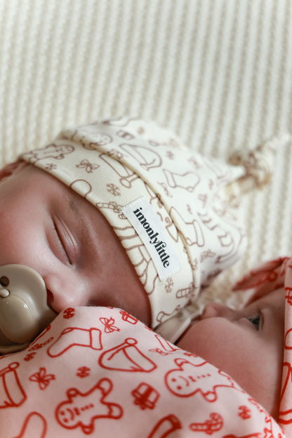 Baby wearing a patterned headband and blanket with a visible brand name.