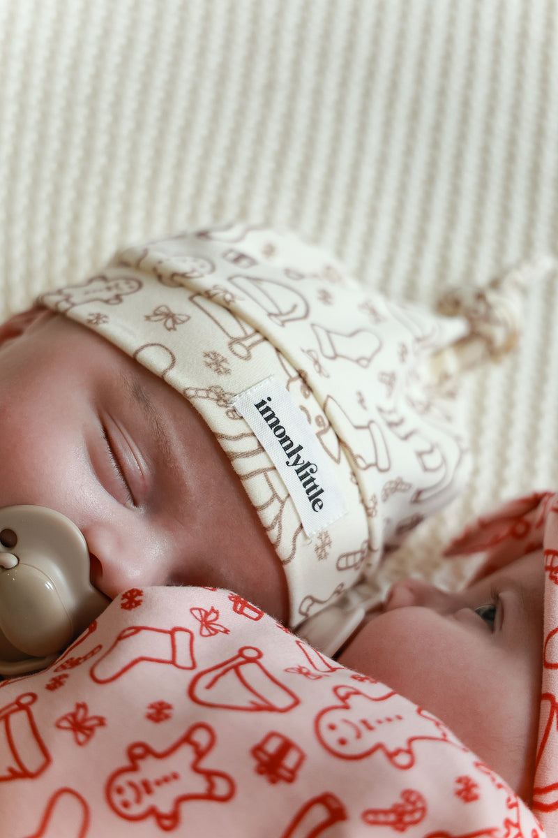 Baby wearing a patterned headband and blanket with a visible brand name.
