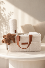 White diaper bag with brown handles and a teddy bear on a white surface.