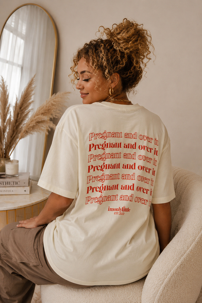 Woman wearing a white t-shirt with red text sitting in a room with a mirror and plant.