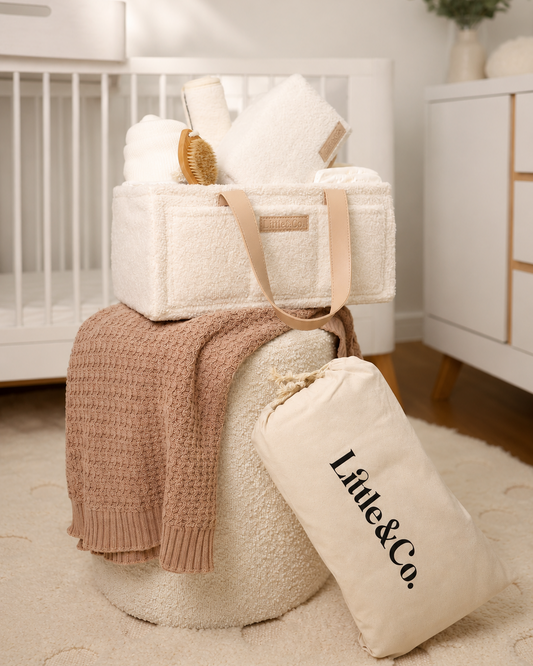 White diaper bag with baby items on a white ottoman in a nursery.