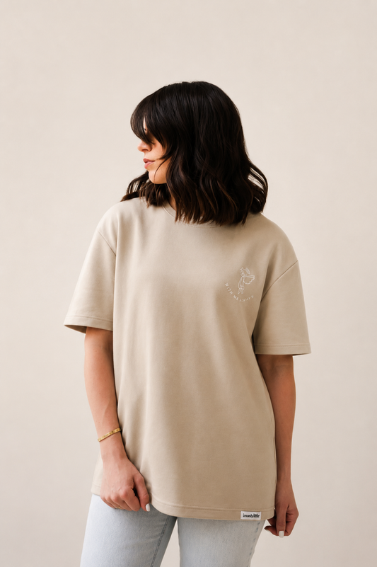 Person wearing a beige t-shirt with a small logo on a plain background