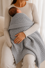 Person holding a baby wrapped in a gray blanket indoors.